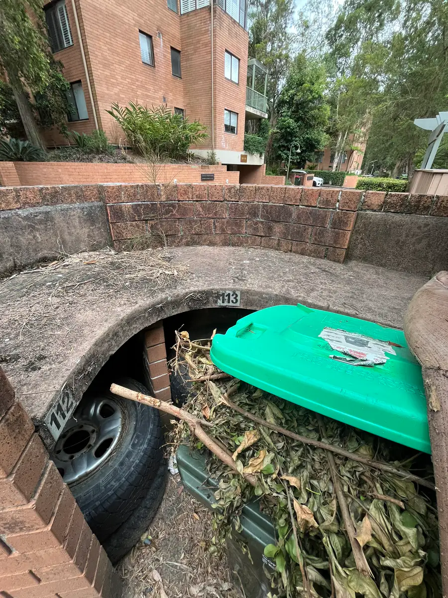 Strata bin enclosure full of green waste and an old tyre, with stained brickwork